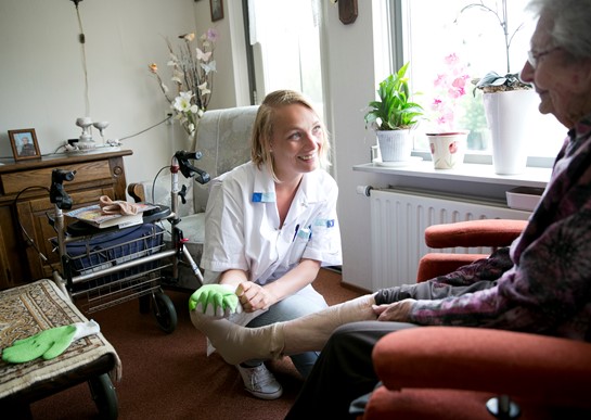 Wijkverpleegkundige trekt steunkous aan bij cliënt