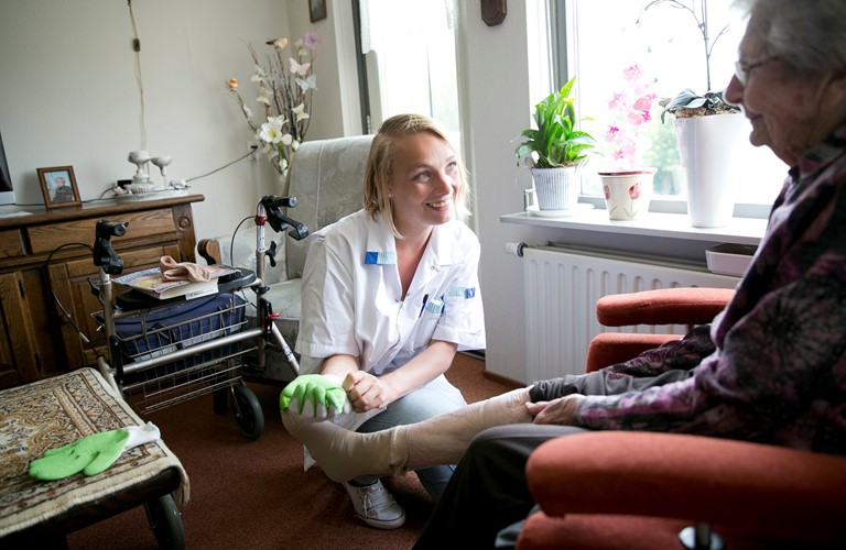 Wijkverpleegkundige trekt steunkous aan bij cliënt